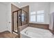 Modern bathroom with a glass-enclosed shower and a soaking tub beneath a window with plantation shutters at 246 Bushney Loop, Mooresville, NC 28115