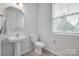 A powder room with a pedestal sink, a white toilet, a window, and neutral decor, with a wood-look floor at 12024 John Newton Dr, Davidson, NC 28036