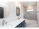 Bathroom with gray tiled shower and double sinks with navy cabinets, quartz counters, and modern round mirrors at 1728 Dallas Ave, Charlotte, NC 28205