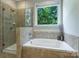 Well-lit bathroom with a tiled shower and tub combination, plus a large window with wooded view at 7916 Deerbridge St, Mint Hill, NC 28227