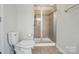 Well-lit bathroom with glass enclosed shower, neutral tile, toilet, and light flooring, with towel rack, and a chrome faucet at 5334 Orchid Bloom Dr, Fort Mill, SC 29707