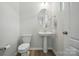This is a half bathroom featuring a pedestal sink, oval mirror, and modern fixtures, toilet, and light wood-look flooring at 5334 Orchid Bloom Dr, Fort Mill, SC 29707