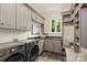 Well-organized laundry room with gray cabinets, modern washer/dryer, sink, window, and a cozy bench area at 1501 Alydar Ct, Waxhaw, NC 28173
