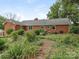 Brick home's backyard featuring a well-manicured lawn and lush landscaping with mature trees and garden beds at 3408 Oak Tree Trl, Matthews, NC 28105