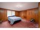 This bedroom features wood paneled walls, pink carpet, and natural light from the window at 5958 Hoover Elmore Rd, Lincolnton, NC 28092