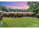 Attractive brick ranch-style home with a pristine lawn, landscaping, and a colorful sunset backdrop at 5424 Doncaster Dr, Charlotte, NC 28211