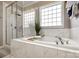 A large bathtub is tiled in white marble adjacent to the glass-enclosed shower in this luxurious bathroom at 129 Hawks Creek Pkwy, Fort Mill, SC 29708