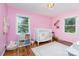 Bright pink Bedroom with hardwood floors, two windows, white trim, and white crib with bookshelves at 4200 Tyndale Ave, Charlotte, NC 28210