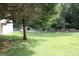 A large, grassy backyard with mature trees, a chain-link fence, and a glimpse of a white outbuilding at 116 Woodbark Ln, Kings Mountain, NC 28086