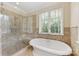 Luxurious bathroom showcasing a freestanding tub, glass-enclosed shower, and natural stone tile work at 1728 Shadow Forest Dr, Matthews, NC 28105
