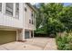 View of a townhouse exterior with a gray garage door and driveway, with a backdrop of lush green trees at 1207 E 36Th St, Charlotte, NC 28205