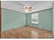 A simple bedroom with light teal walls, wood floor and ceiling fan, with a sunny window view at 1532 Buffalo Shoals Rd, Claremont, NC 28610