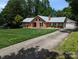 Charming brick home featuring a well-manicured lawn, mature trees, and an expansive driveway at 8007 Caldwell Rd, Harrisburg, NC 28075