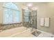 Bright bathroom featuring a soaking tub with stone accents and a glass-enclosed shower at 9137 Brightleaf Pl, Charlotte, NC 28269