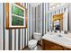 Cozy bathroom featuring striped wallpaper, a white toilet and sink, and a wood-trimmed window at 328 Pamela St, Gastonia, NC 28054