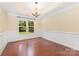 This dining room boasts classic wainscoting, hardwood floors, and a modern chandelier above a window overlooking the garden at 10129 Loch Lomond Dr, Charlotte, NC 28278