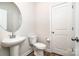 Well-lit powder room with a modern pedestal sink and a round mirror next to a white paneled door at 7012 Bryce Ave, Charlotte, NC 28217