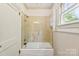 Bright bathroom featuring a tub-shower combo with glass door and beige tile surround, accented with white wainscoting at 805 S Main St, Mount Holly, NC 28120