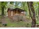 Quaint cabin featuring a covered porch, lattice skirting, and natural wood siding nestled in a wooded area at 715 White Oaks Cir, Monroe, NC 28110