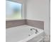 Close up of a pristine white bathtub with chrome fixtures and neutral tile backsplash underneath a frosted glass window at 171 Old Harbor Dr, Mount Gilead, NC 27306