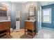 Dual vanity bathroom with blue accent wall, wood-trimmed mirrors, storage cabinet, and tile flooring at 5701 Silver Eagle Dr, Charlotte, NC 28214