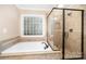 Luxurious bathroom with soaking tub, glass enclosed shower, and block glass window at 6300 Morehead Rd, Harrisburg, NC 28075