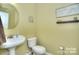 Half bathroom with a round mirror, pedestal sink, and a painting on the wall at 9792 Ravenscroft Nw Ln, Concord, NC 28027
