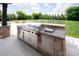 A stone outdoor kitchen features stainless steel appliances and bar seating overlooking a well-manicured backyard at 11008 Strike The Gold Ln, Waxhaw, NC 28173