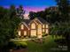 Elegant brick home with manicured lawn, lush landscaping, and warm, inviting exterior lighting at 9514 Hayenridge Ct, Huntersville, NC 28078