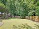 Expansive backyard featuring lush green grass, mature trees, a wooden fence, and a charming playhouse at 7639 Winterset Dr, Charlotte, NC 28270