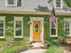 Close-up of the green home's entryway with an orange door, American flag, and potted plants, creating a welcoming entrance at 7639 Winterset Dr, Charlotte, NC 28270
