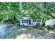 Charming single-story home with a brick foundation, black shutters, and a vibrant red front door nestled among mature trees at 828 Williams St, Gastonia, NC 28052