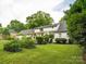 Wide backyard view of home and garden with lush green lawn, mature trees, and planting beds at 2032 Greenbrook Pkwy, Matthews, NC 28104