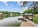 Waterfront dock with covered boat slip, featuring multiple boats and a serene lake backdrop under a partly cloudy sky at 138 Ardmore Pl, Mooresville, NC 28117