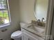 Cozy half-bath with granite countertop, stainless steel faucet, round mirror, and window at 11021 Scrimshaw Ln, Charlotte, NC 28215