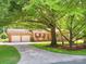Inviting brick ranch-style house featuring a long driveway, attached two-car garage, rocking chairs, and mature trees at 10728 Forest Dr, Matthews, NC 28105