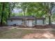 A single story house with a grey wood siding and a small entry porch surrounded by mature shade trees at 5143 Delivau Dr, Charlotte, NC 28215