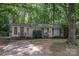Charming single-story home with a gray facade, a concrete driveway, and mature trees in a wooded setting at 5143 Delivau Dr, Charlotte, NC 28215