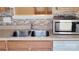 Close-up of the kitchen sink area, showcasing stainless steel sink, microwave, mosaic backsplash, and white appliances at 12450 Stone Garden Dr, Huntersville, NC 28078