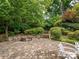 Paver patio with a stone fire pit surrounded by lush trees and a beautiful landscaped backyard at 9212 John Hawks Rd, Cornelius, NC 28031