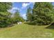 A backyard features a lush lawn with mature trees under a blue sky with white clouds at 7785 Crestwood Dr, Kannapolis, NC 28081