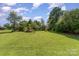 View of the spacious backyard featuring well-maintained grass and lots of mature shade trees at 7785 Crestwood Dr, Kannapolis, NC 28081