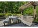 Outdoor dining area with a stone patio, built-in grill, and a wooden pergola surrounded by mature trees at 17537 Caddy Ct, Charlotte, NC 28278