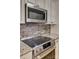 Close-up of a stainless steel range and microwave with granite countertops and tile backsplash at 413 Farm Branch Dr, Fort Mill, SC 29715