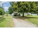 A cozy, light-colored house nestled among lush trees with a gravel driveway at 201 Oakland Dr, Lowell, NC 28098