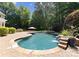 Backyard features a pool with rock waterfall, brick patio, lush greenery and wooded views at 4536 Rustling Woods Dr, Denver, NC 28037
