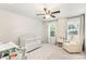 Bright bedroom featuring a ceiling fan, a crib with white accents, and a cozy chair near a window at 15636 Oleander Dr, Charlotte, NC 28278