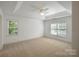 Spacious bedroom featuring neutral carpet, tray ceiling, ceiling fan, and windows with green foliage views at 8900 Cumbria Ct, Huntersville, NC 28078