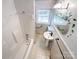 Bright bathroom featuring a white tiled shower-tub combo, pedestal sink, floral wall decor, and window at 310 E Houston St, Monroe, NC 28112