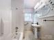 Traditional bathroom with a shower-tub, pedestal sink, floral wall decor, and storage shelves at 310 E Houston St, Monroe, NC 28112